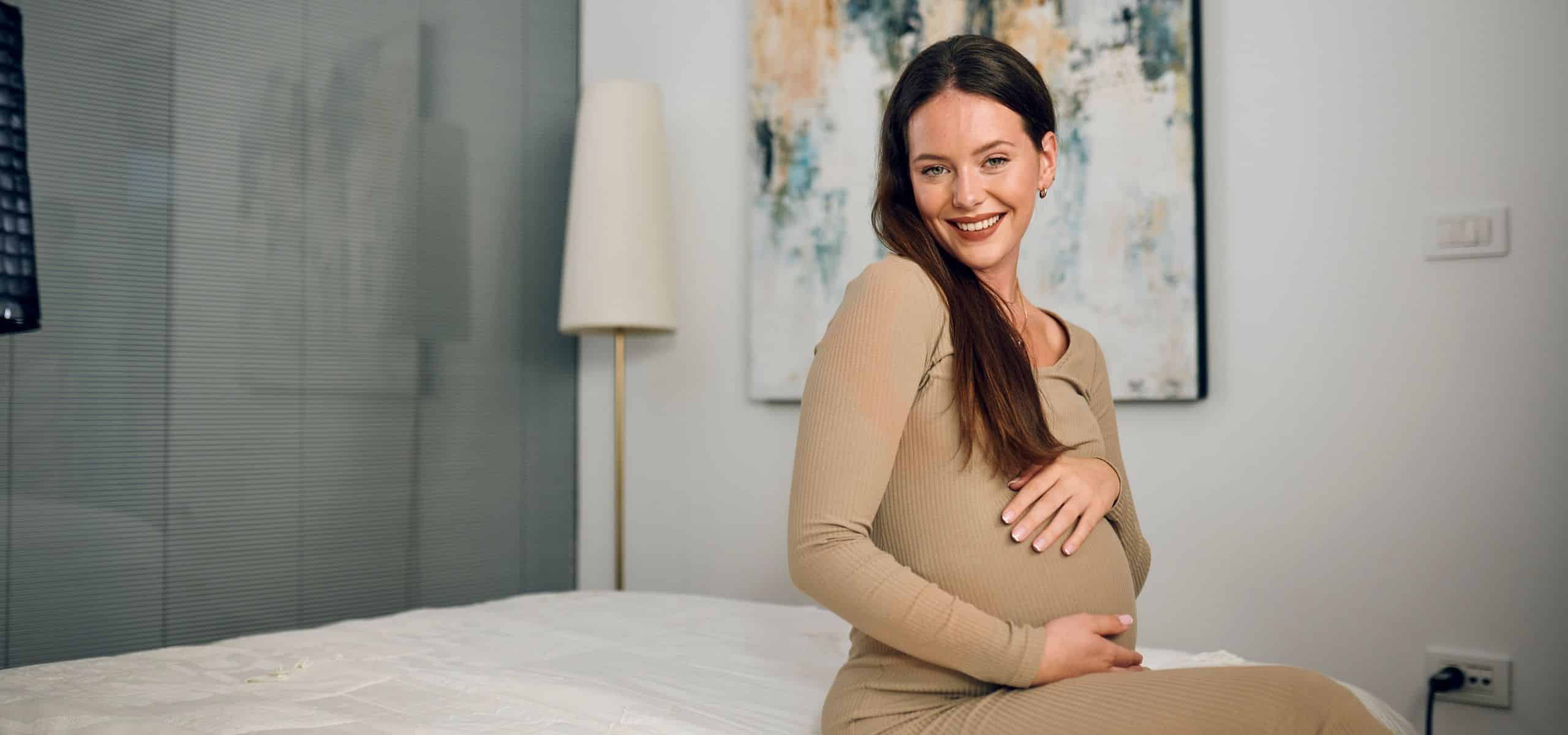 Trudnica sjedi na krevetu i miluje svoj trbuh
