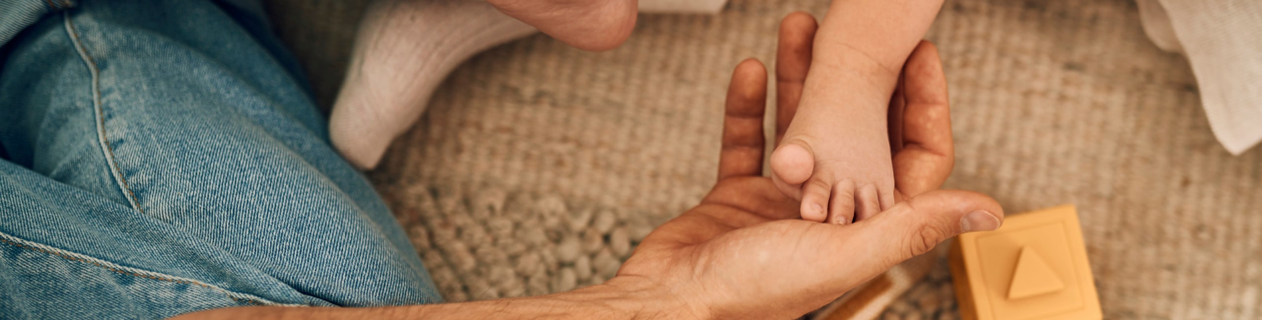 Tata drži bebino stopalo, mekani tepih i igračke