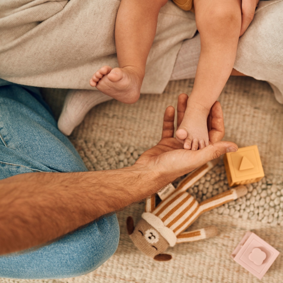 Tata drži bebino stopalo, mekani tepih i igračke